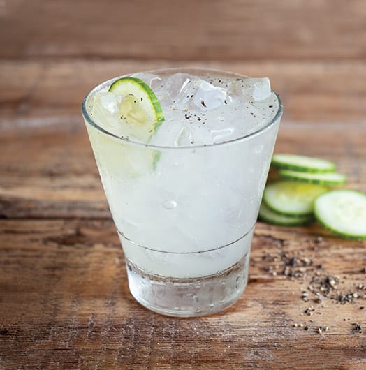 A signature cocktail displayed with a cut up cucumber in the background